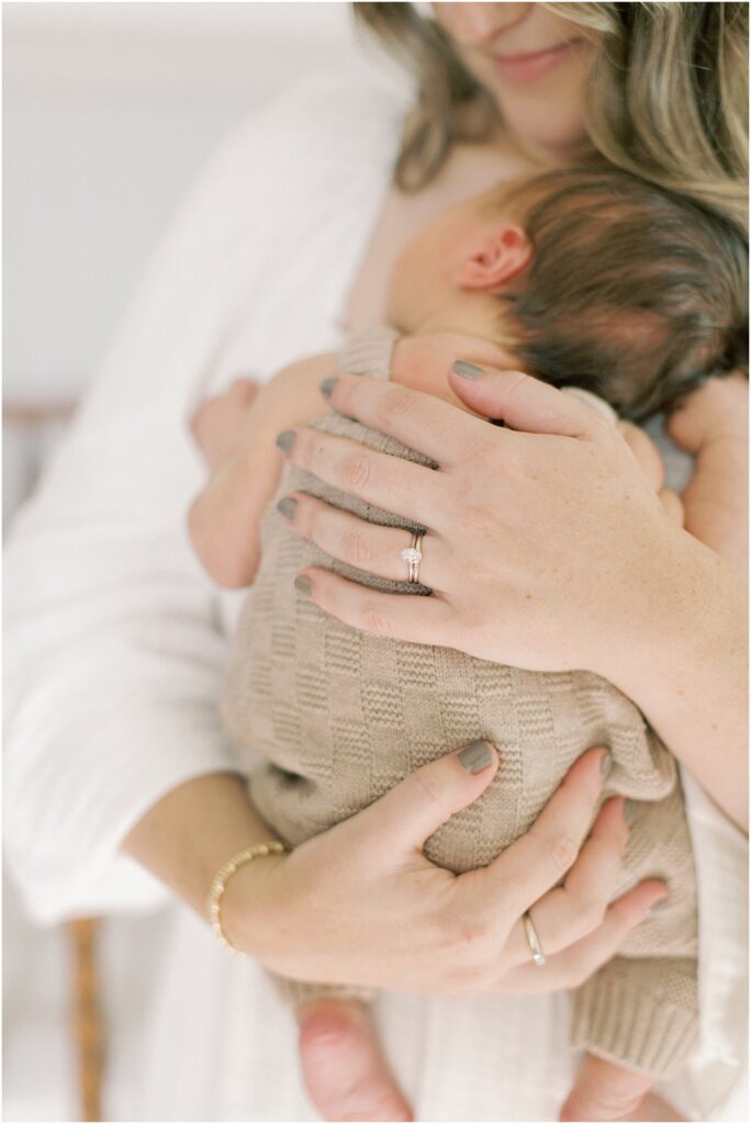 details of a mother's hands on her newborn son showing her rings on her fingers.