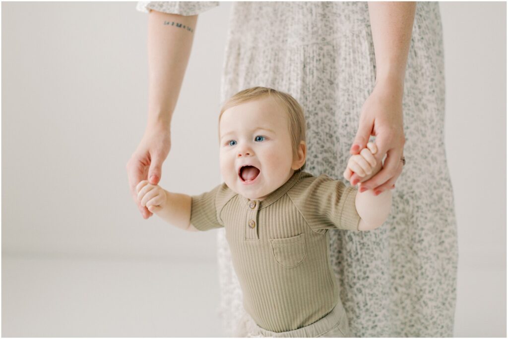Toddler holding his mama's hands at his first birthday session