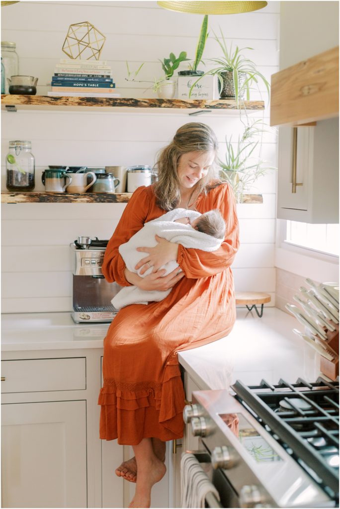 Mother sitting on kitchen counter holding baby at newborn session at home