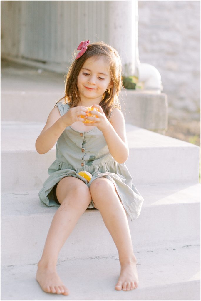 Little girl sitting on stoop eating oranges