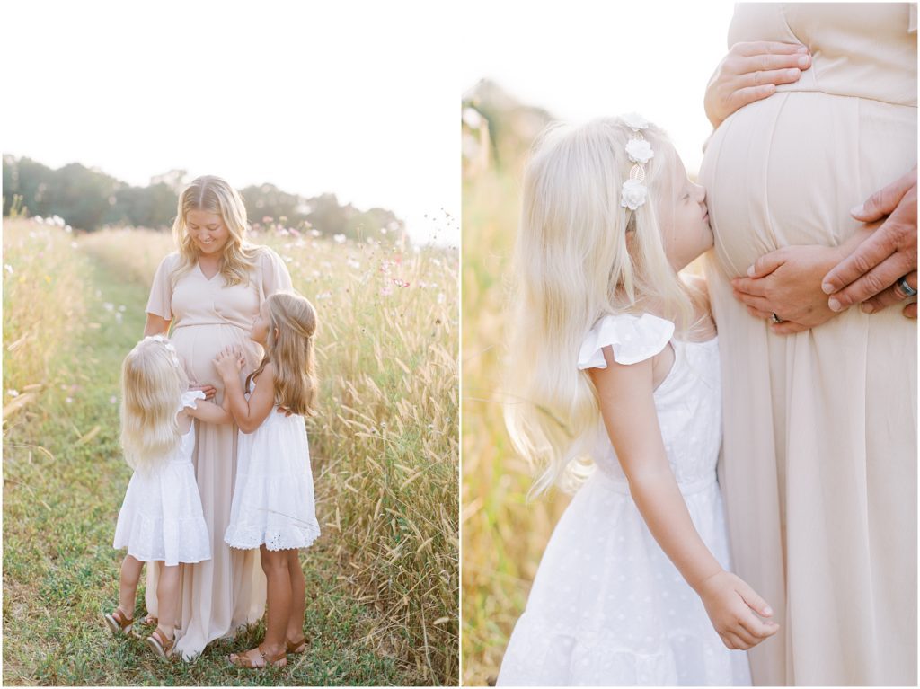 Girls hugging and kissing mom's pregnant belly in flower field maternity session