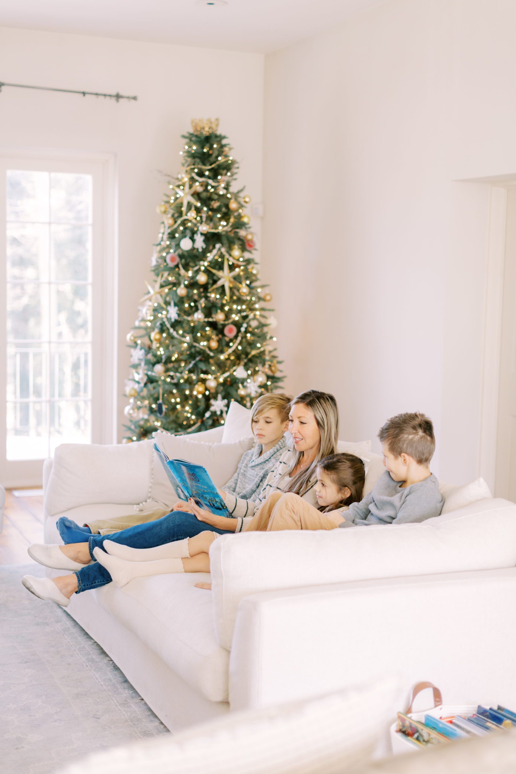 Momma reading a Christmas story to her kids by the tree