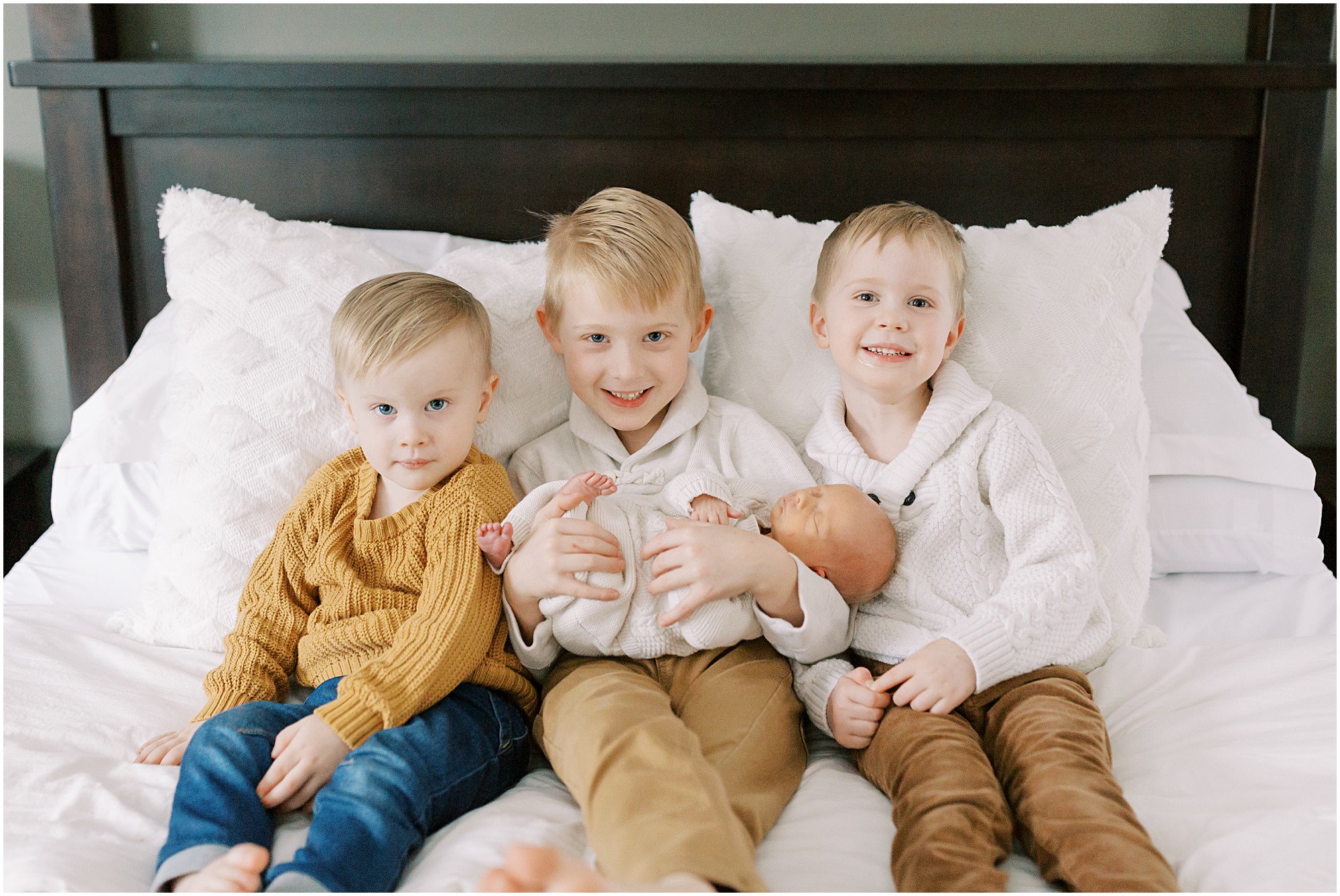 Boys with their newborn baby brother on a bed
