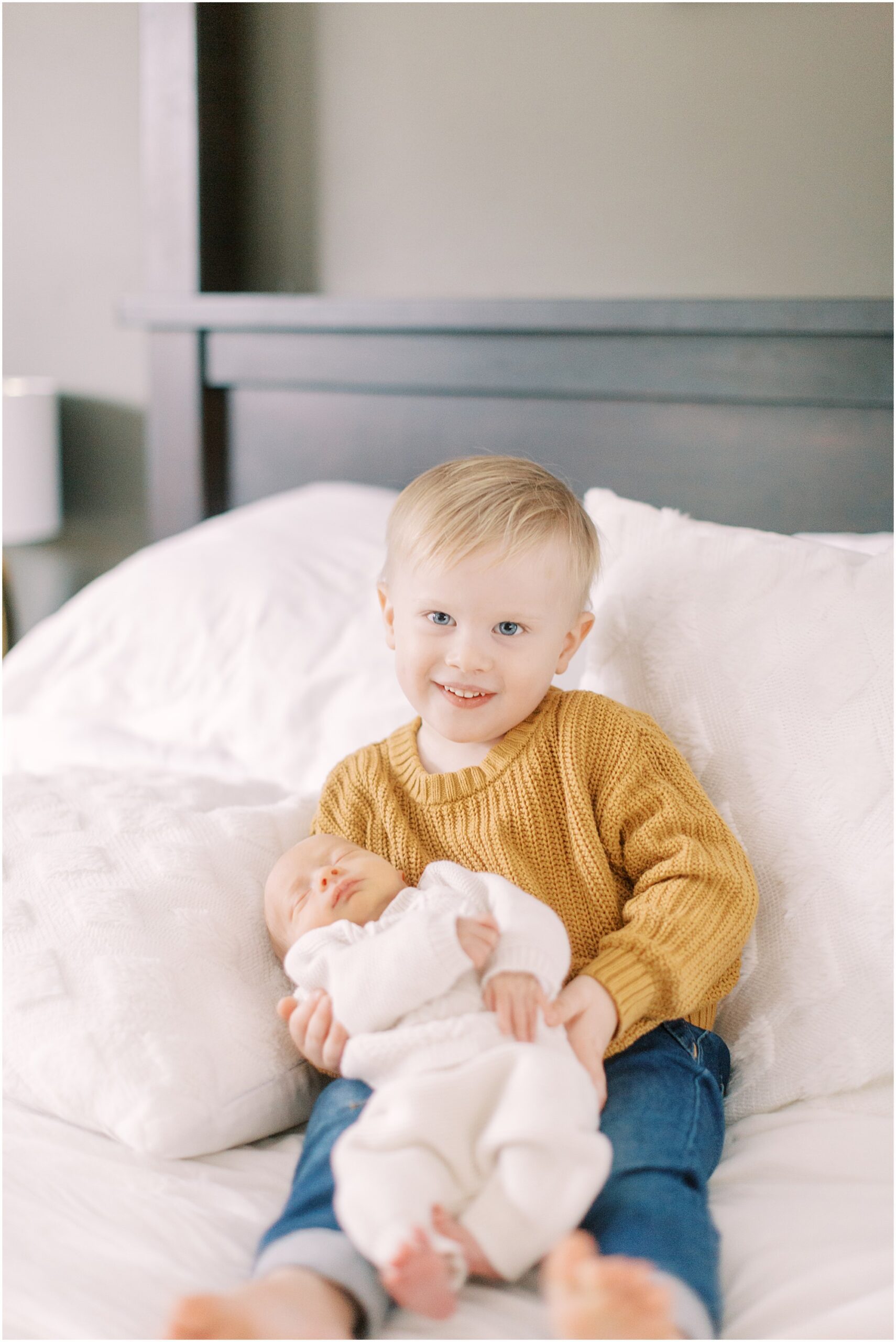 Toddler boy holding newborn baby brother at a newborn session with boys