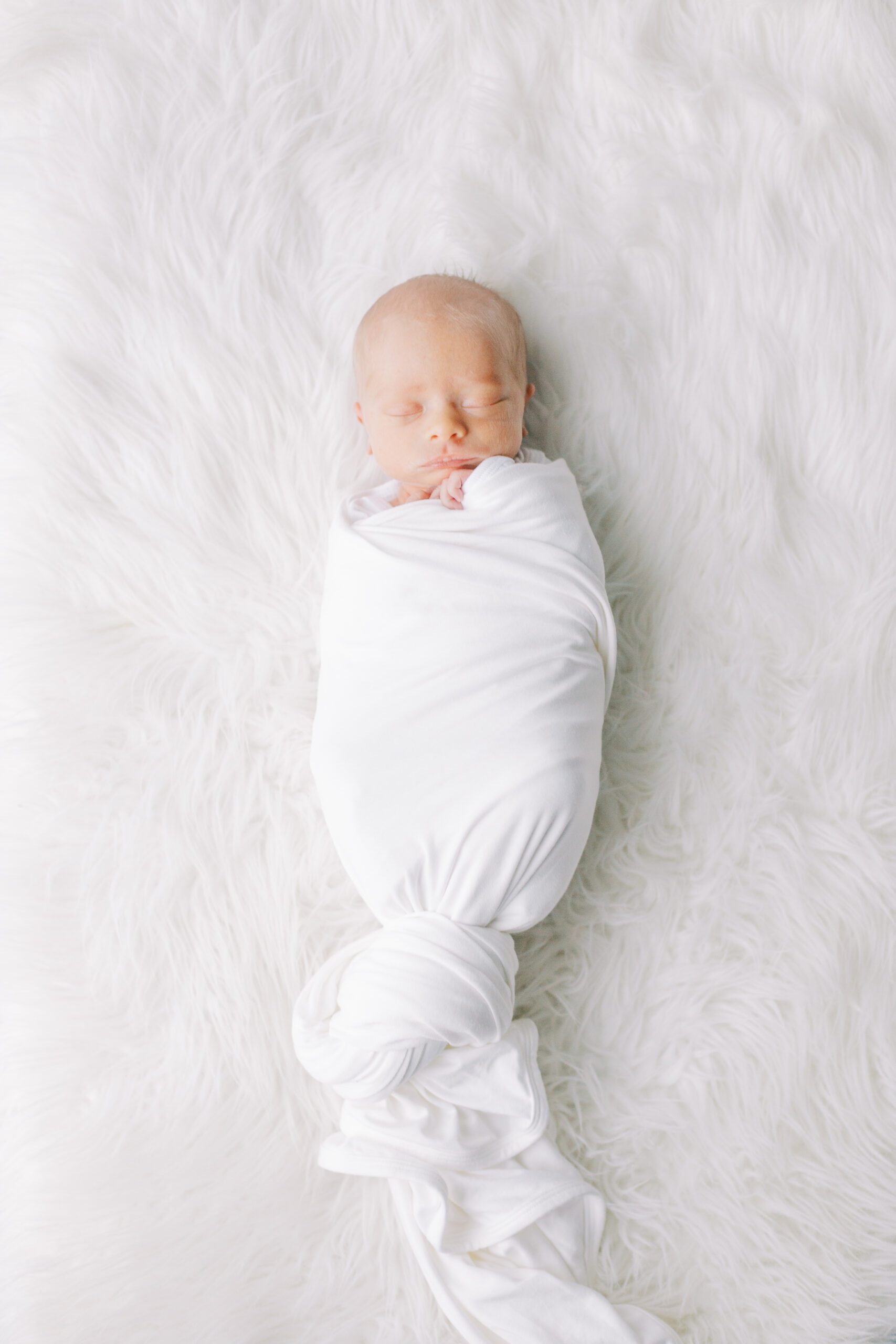 Newborn baby wrapped in white swaddle blanket on white fur background in Two Favorite Companies for Baby Items