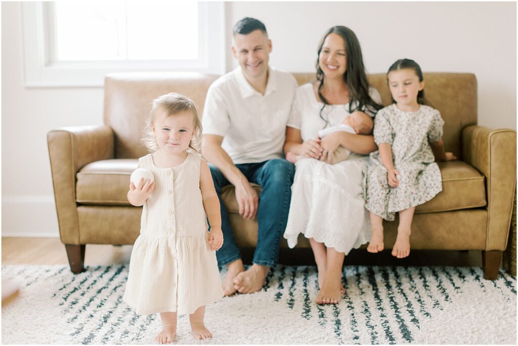 Family sitting on the couch looking at a toddler during their newborn photography session