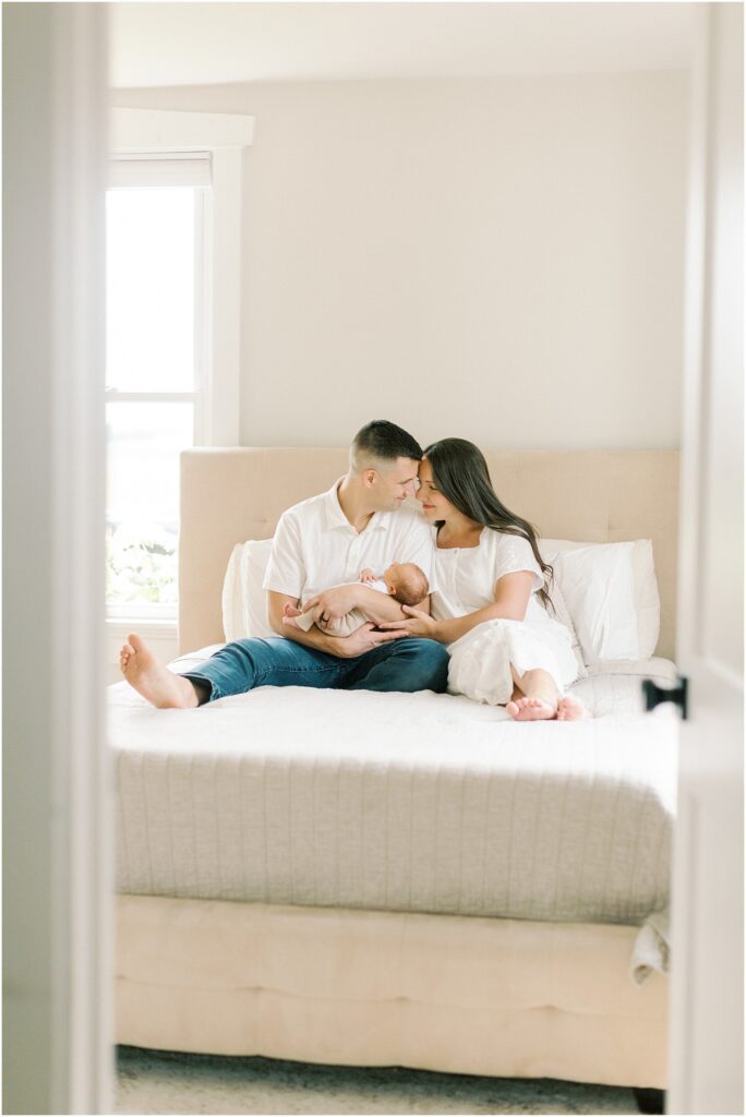 Parents sitting on their bed holding their newborn son with Chester County PA Newborn Photographer Angelique Jasmin Photography