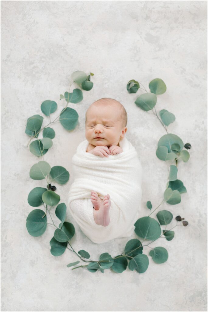 Newborn flat lay: Newborn laying on styling mat wrapped in white and surround by eucalyptus with Angelique Jasmin Photography