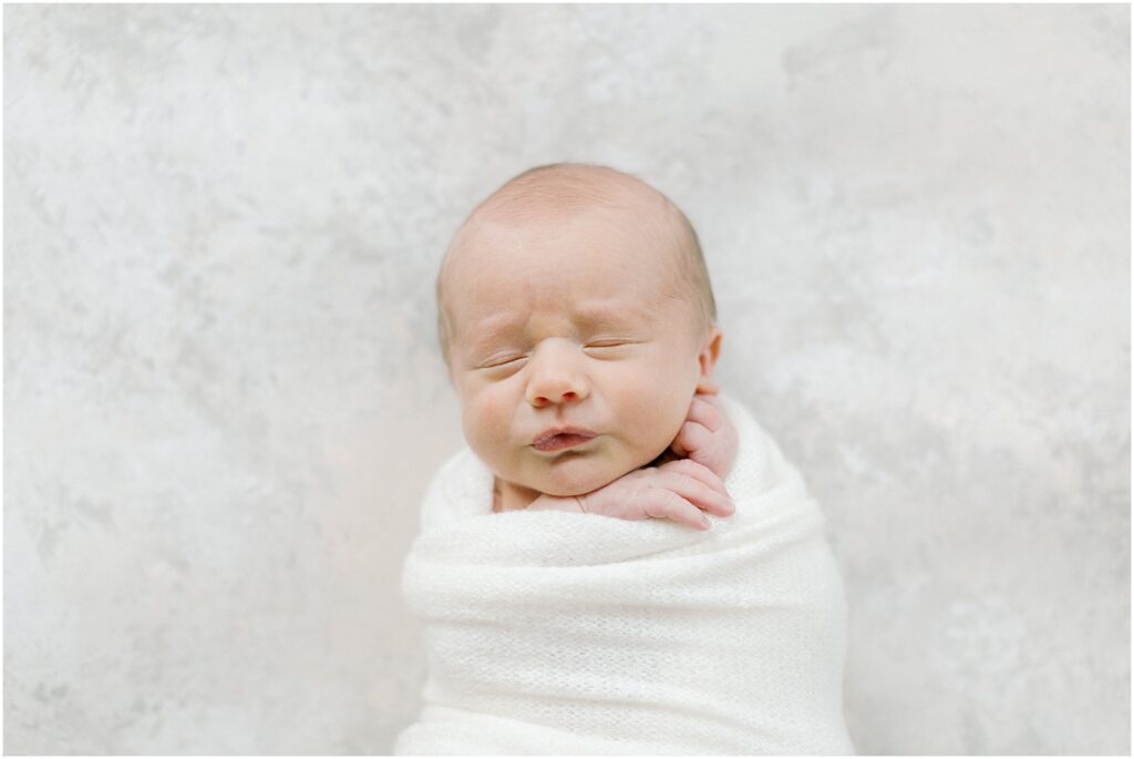 Newborn baby wrapped in white on styling mat painted by April Raymond
