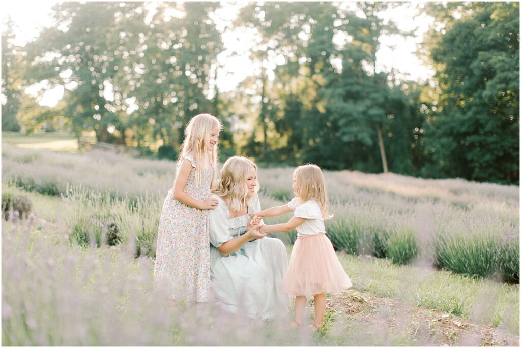 A mother and daughters interacting at a lavender field photo session with Angelique Jasmin Photography