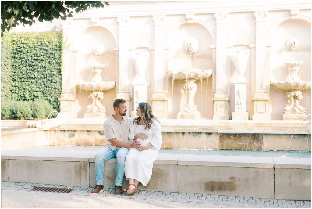 Couple sitting by a pool and fountains at a maternity session