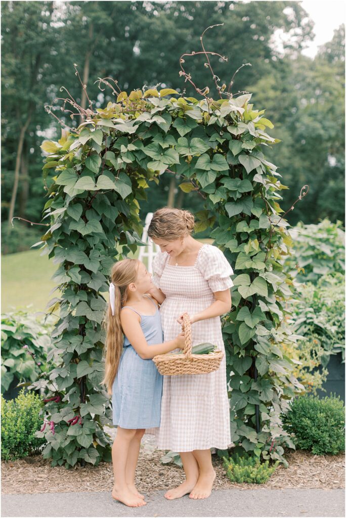 Mother and daughter standing together next to a garden arbor in motherhood and gardening with Angelique Jasmin Photography