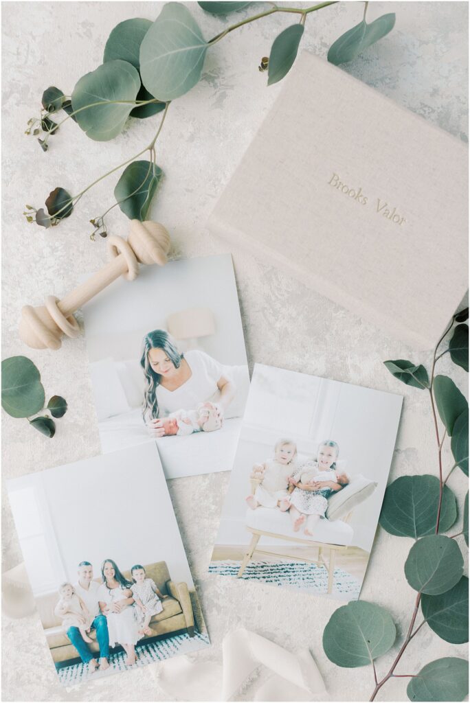 Photography flat lay of newborn products including deep matte prints with eucalyptus, a wooden rattle and a linen photo storage box with Angelique Jasmin Photography