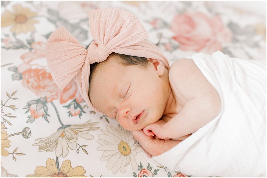 Newborn baby girl with large pink bow on her head on a floral background with Angelique Jasmin Photography, an Elizabethtown PA Newborn Photographer.