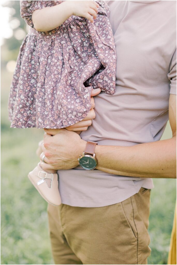 Up close details of man's watch and his hands as he holds his toddler daughter. 