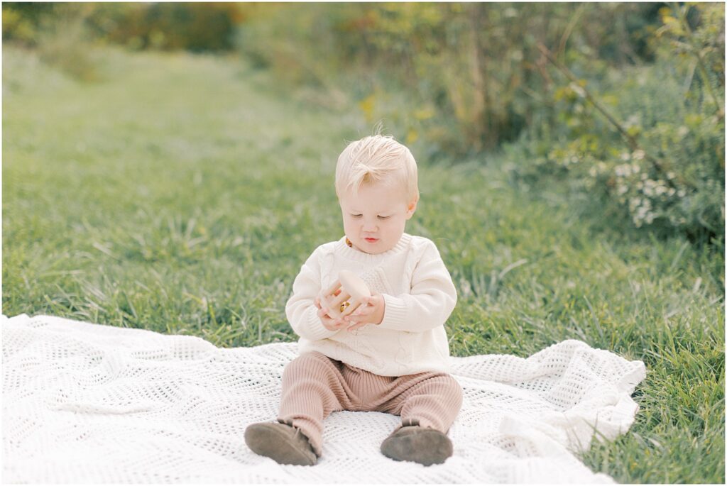 Baby Boy sitting on a white blanket playing with wooden toy.