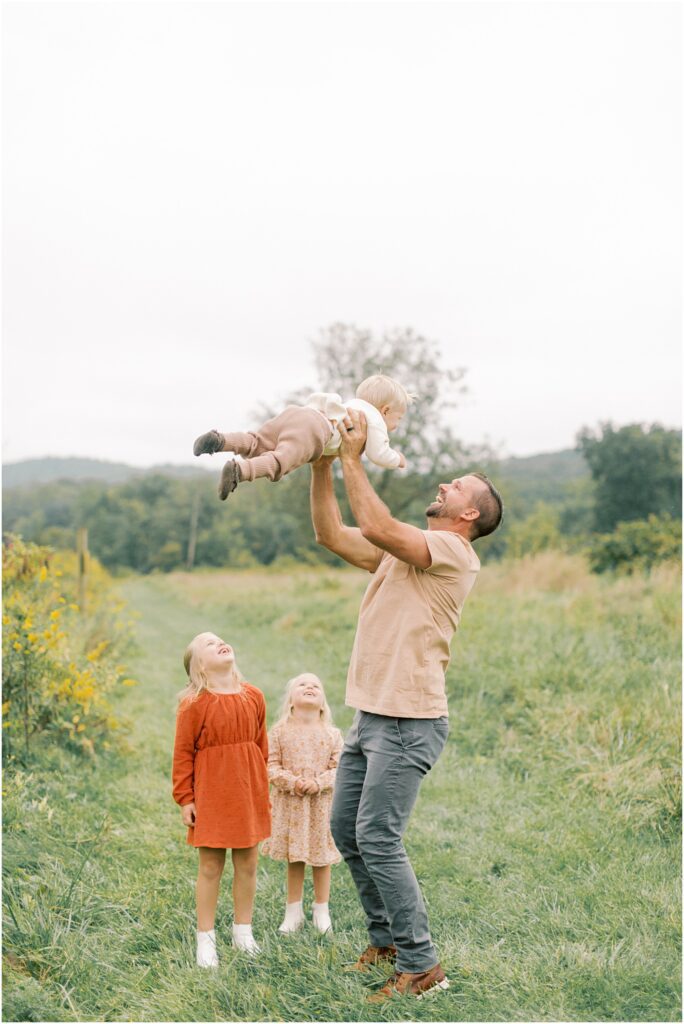 Father lifting his son into the air while his little daughters are watching