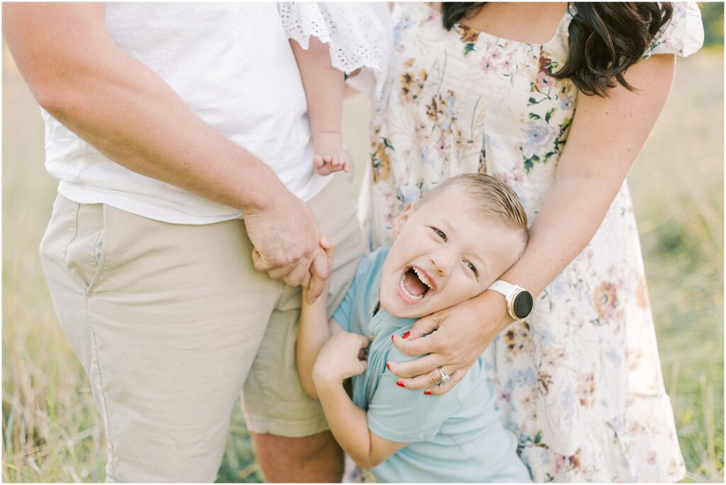 Young boy laughing with his parents hands and arms around him