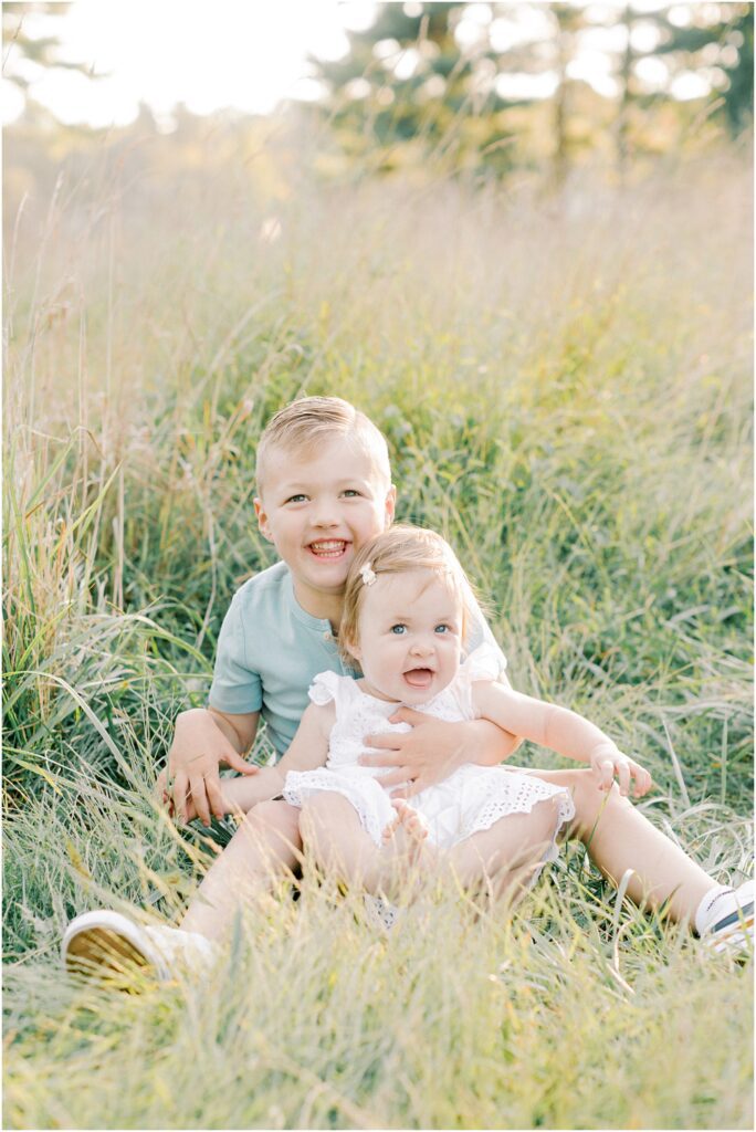 Brother holding his sister while sitting in the long grasses.