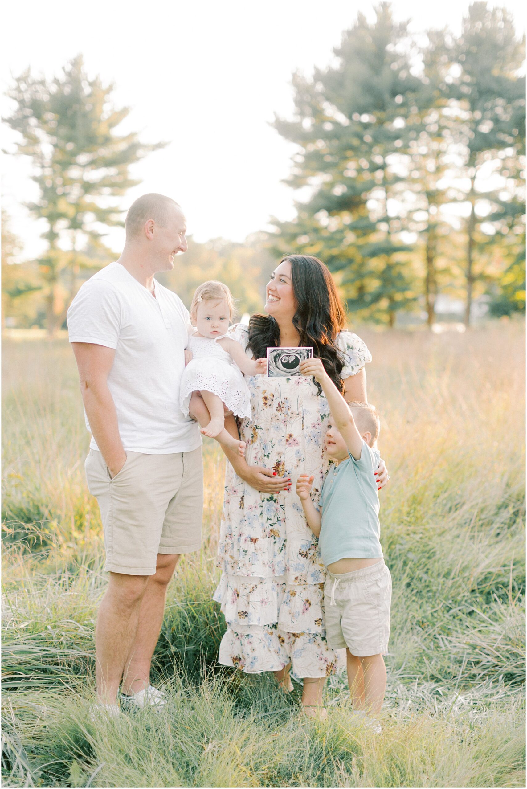 Family in a field with an ultrasound photo in Lancaster PA Pregnancy Announcement