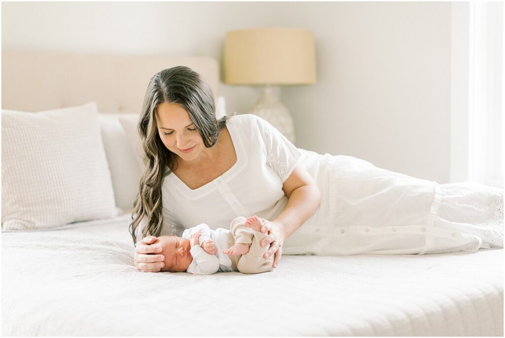 Mother laying on a bed in a neutral bedroom in when to book newborn photos