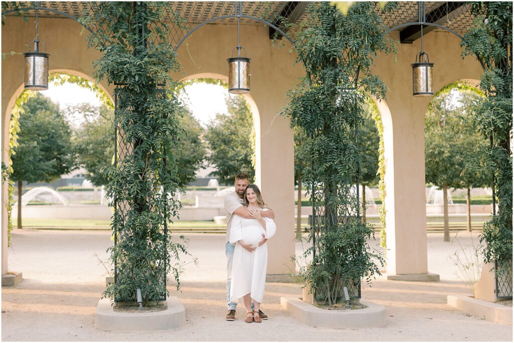 Couple standing under vine covered arches at Longwood Gardens at their maternity session.