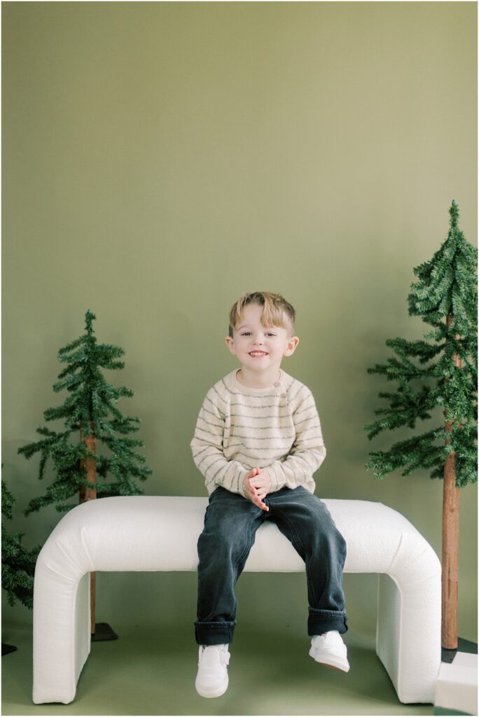 Little boy sitting on a bench in a Christmas mini set up with trees.