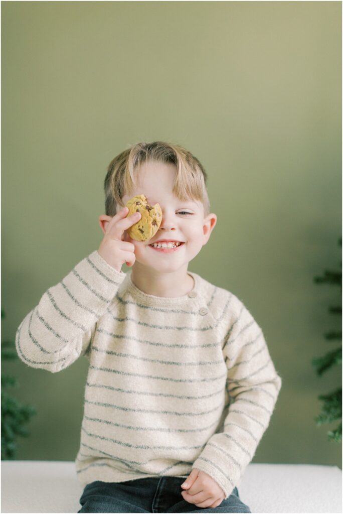 Young boy holding a chocolate chip cookie to one eye. 