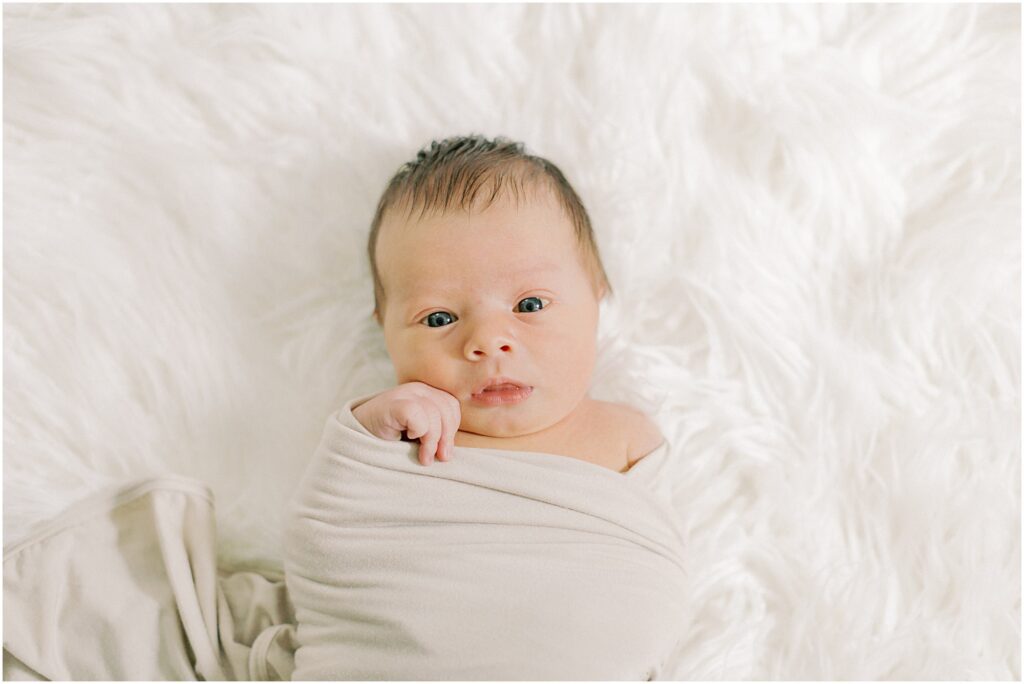 Newborn baby boy laying on a white fuzzy backdrop.
