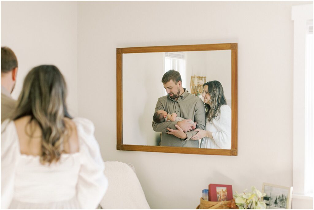 Reflection of parents looking at their baby in the mirror of the nursery
