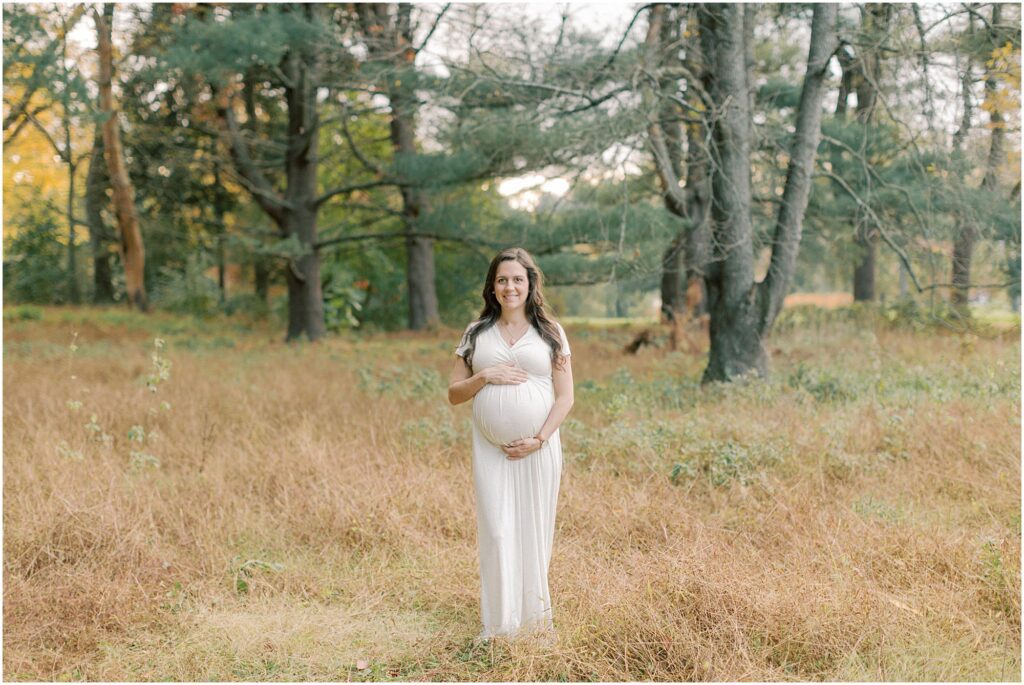 Pregnant woman standing in the woods holding her pregnant belly in a Lancaster County Central Park Maternity Session