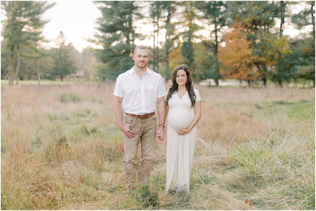 Expecting couple standing side by side holding hands in a field